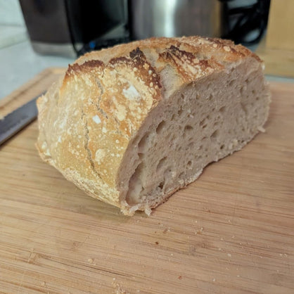 A rustic loaf of artisan bread, sliced to show its airy crumb, resting on a wooden cutting board.
